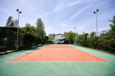 Campo da tennis al Camping Nautic Almata, villaggio turistico in Catalogna, Spagna, circondato da alberi.