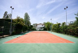 Campo da tennis al Camping Nautic Almata, villaggio turistico in Catalogna, Spagna, circondato da alberi.