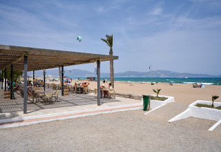 Strandudsigt fra Camping Nautic Almata i Catalonien, Spanien med udendørs café og folk der slapper af.
