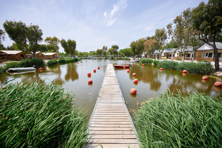 Houten steiger over een vijver met bungalows en groen bij Camping Nautic Almata in Catalonië, Spanje.