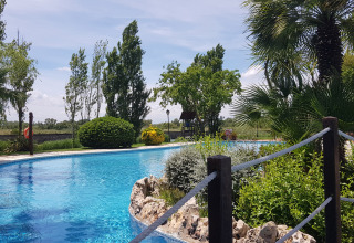 Piscina all’aperto al Camping Nautic Almata in Catalogna, Spagna, circondata da alberi e piante verdi.