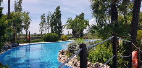 Piscina all’aperto al Camping Nautic Almata in Catalogna, Spagna, circondata da alberi e piante verdi.