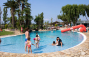 Familier nyder poolen med børn på Camping Nautic Almata feriepark i Catalonien, Spanien, på en solrig dag.