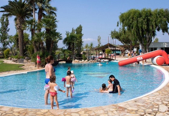Familier nyder poolen med børn på Camping Nautic Almata feriepark i Catalonien, Spanien, på en solrig dag.