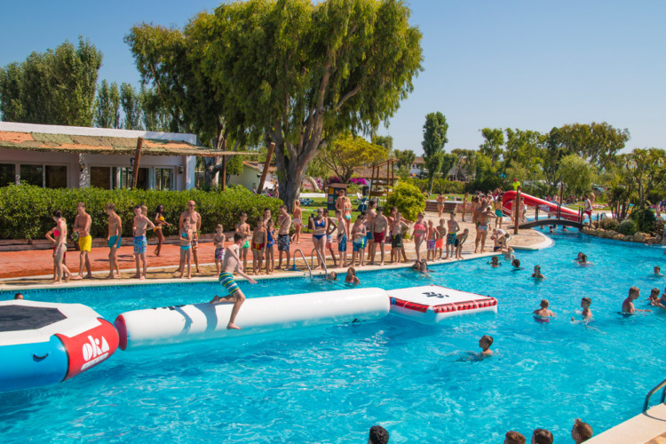 Kinderen en volwassenen genieten van waterpret op springkussens in het zwembad van Camping Nautic Almata.