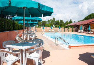 Swimmingpool med hvide stole, borde og blå parasoller på Camping Pian Di Boccio, Umbrien, Italien.