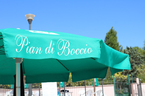Ombrellone verde con la scritta 'Pian di Boccio' nel campeggio Pian Di Boccio, parco vacanze in Umbria, Italia.