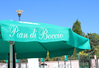 Groene parasol met opschrift 'Pian di Boccio' op Camping Pian Di Boccio vakantiedomein in Umbrië, Italië.