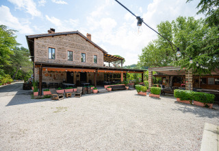 Vista esterna di edificio in pietra e cortile con sedute al Camping Pian Di Boccio, Umbria, Italia.