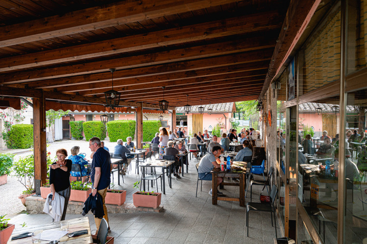 Overdekt buitenterras van Camping Pian Di Boccio in Umbrië, Italië, met etende gasten aan tafels.
