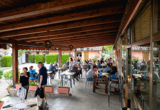 Overdekt buitenterras van Camping Pian Di Boccio in Umbrië, Italië, met etende gasten aan tafels.