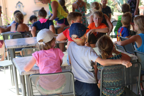 Niños sentados en mesas disfrutando actividades al aire libre en Camping Pian Di Boccio, Umbría, Italia.
