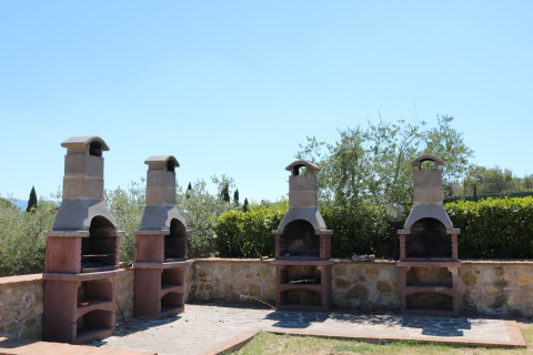 Area barbecue all'aperto con quattro griglie in pietra al Camping Pian Di Boccio, circondata dal verde.