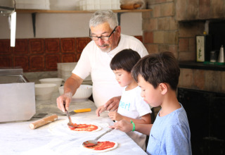 Oudere man en twee kinderen maken samen pizza in de keuken van Camping Pian Di Boccio in Umbrië, Italië.