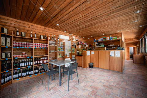 Recepción y tienda interior con estanterías de madera y vinos en Camping Pian Di Boccio, Umbría, Italia.