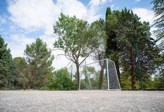 Voetbaldoel op een sportterrein met hoge bomen en omheining bij Camping Pian Di Boccio, Umbrië, Italië.