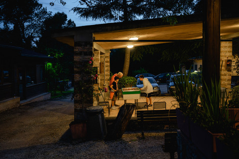 Due persone giocano a calcio balilla la sera sotto una terrazza coperta al Camping Pian Di Boccio, Umbria, Italia.