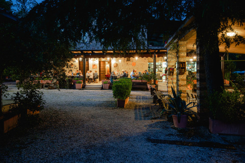 Vista nocturna del restaurante en Camping Pian Di Boccio, un parque vacacional en Umbría, Italia, con comensales afuera.