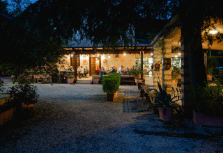 Vista nocturna del restaurante en Camping Pian Di Boccio, un parque vacacional en Umbría, Italia, con comensales afuera.