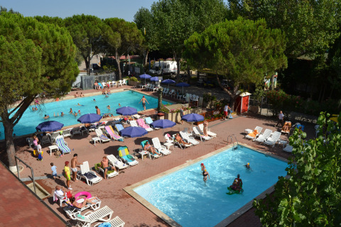 Famiglie si rilassano tra piscine, lettini e ombrelloni al Camping Punta Navaccia, parco vacanze in Umbria, Italia.