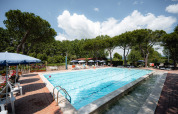 Swimmingpool med liggestole og parasoller på Camping Punta Navaccia i Umbrien, Italien, omgivet af træer.