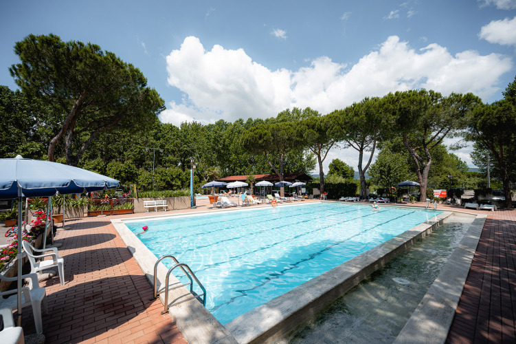 Poolbereich mit Liegestühlen und Sonnenschirmen im Camping Punta Navaccia, Umbrien, Italien, umgeben von Bäumen.
