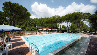 Piscina exterior con tumbonas y sombrillas en Camping Punta Navaccia, Umbría, Italia, rodeada de árboles.