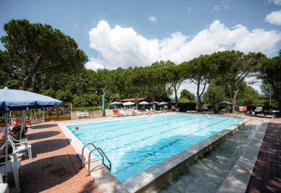 Poolbereich mit Liegestühlen und Sonnenschirmen im Camping Punta Navaccia, Umbrien, Italien, umgeben von Bäumen.