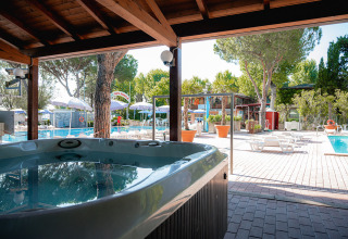 Buitenspa en zwembad met ligstoelen onder bomen bij Camping Punta Navaccia vakantiepark in Umbrië, Italië.