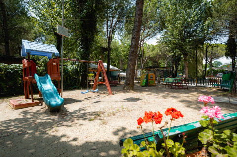 Parco giochi con scivolo, altalene e fiori in primo piano al Camping Punta Navaccia in Umbria, Italia.