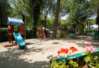Spielplatz mit Rutsche, Schaukeln und Blumen im Vordergrund auf dem Camping Punta Navaccia in Umbrien, Italien.