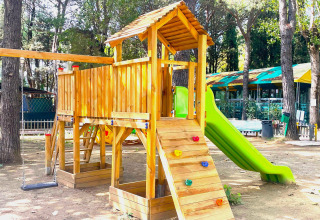 Een speeltuin met houten speelhuisje, glijbaan en schommel bij Camping Punta Navaccia in Umbrië, Italië.