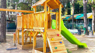 Un parque infantil con casa de madera, tobogán y columpios en Camping Punta Navaccia en Umbría, Italia.