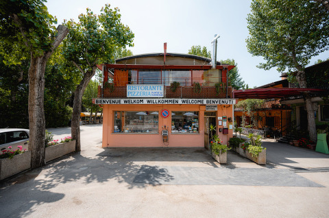 Ingresso al Camping Punta Navaccia con ristorante e ufficio, circondato da alberi in Umbria, Italia.