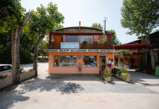 Ingang van Camping Punta Navaccia met restaurant en kantoor, omgeven door bomen in Umbrië, Italië.