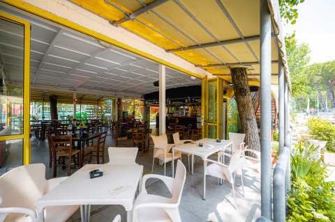Zona de comedor al aire libre con sillas blancas y de madera en Camping Punta Navaccia en Umbría, Italia.