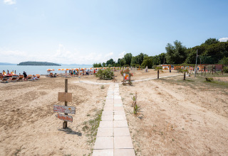Camping Punta Navaccia in Umbrië, Italië, met zandstrand, oranje parasols en vakantiegangers bij het meer.