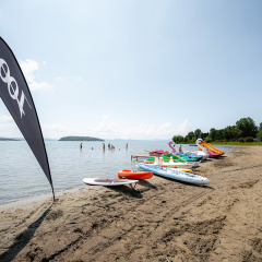 Playa en Camping Punta Navaccia, Umbría, Italia, con hidropedales y tablas de paddle surf en un día soleado.