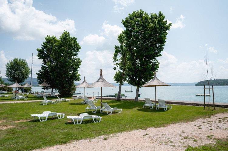 Grüner Campingplatz am See mit Liegestühlen und Strohdächern in Camping Punta Navaccia, Umbrien, Italien.