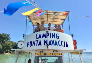 Groep mensen op een boot met Camping Punta Navaccia bord, genieten van de zon op een meer in Umbrië, Italië.