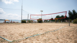 Cancha de voleibol de arena en Camping Punta Navaccia, Umbría, Italia, con vistas al lago y personas descansando.