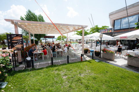Area pranzo all'aperto al Camping Punta Navaccia in Umbria, Italia, con ospiti sotto una pergola e ombrelloni.