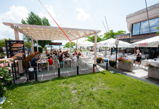 Buiten eethoek op Camping Punta Navaccia in Umbrië, Italië, met gasten onder een pergola en parasols.