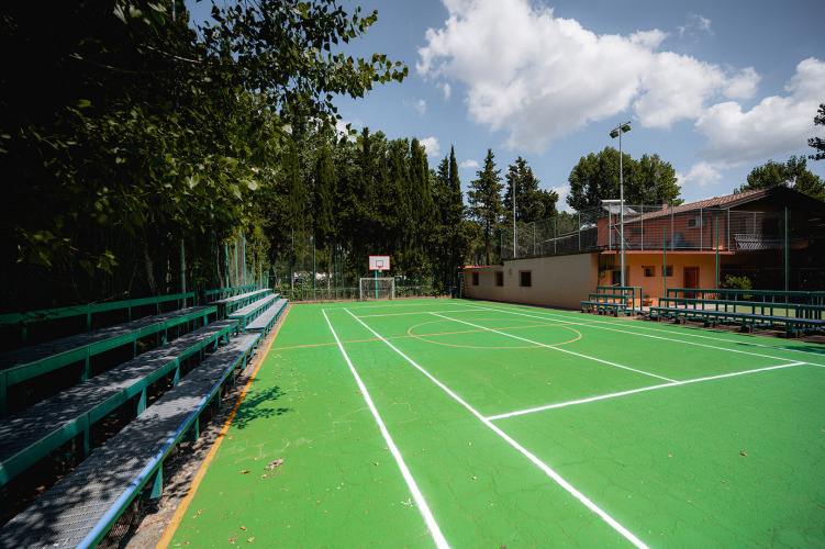 Grüner Basketballplatz mit Tribünen im Freien im Ferienpark Camping Punta Navaccia in Umbrien, Italien.