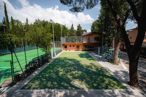 Campi sportivi all'aperto e campo da tennis con alberi e edifici presso Camping Punta Navaccia in Umbria, Italia.