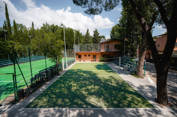 Sportplätze im Freien und Tennisplatz mit grünen Bäumen und Gebäuden auf Camping Punta Navaccia in Umbrien, Italien.