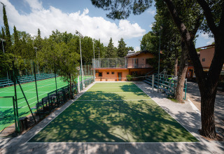 Udendørs sportshaller og tennisbane med grønne træer og bygninger på Camping Punta Navaccia i Umbrien, Italien.