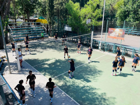 Giovani che giocano a pallavolo su un campo all'aperto circondato da alberi al Camping Punta Navaccia, Umbria.