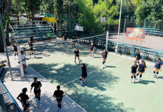 Jongeren spelen volleybal op een openluchtveld omringd door bomen bij Camping Punta Navaccia, Umbrië.