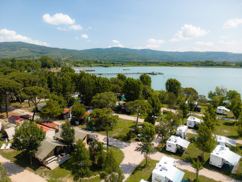 Vista aerea di Camping Punta Navaccia in Umbria, Italia, con roulotte, lago e colline verdeggianti.